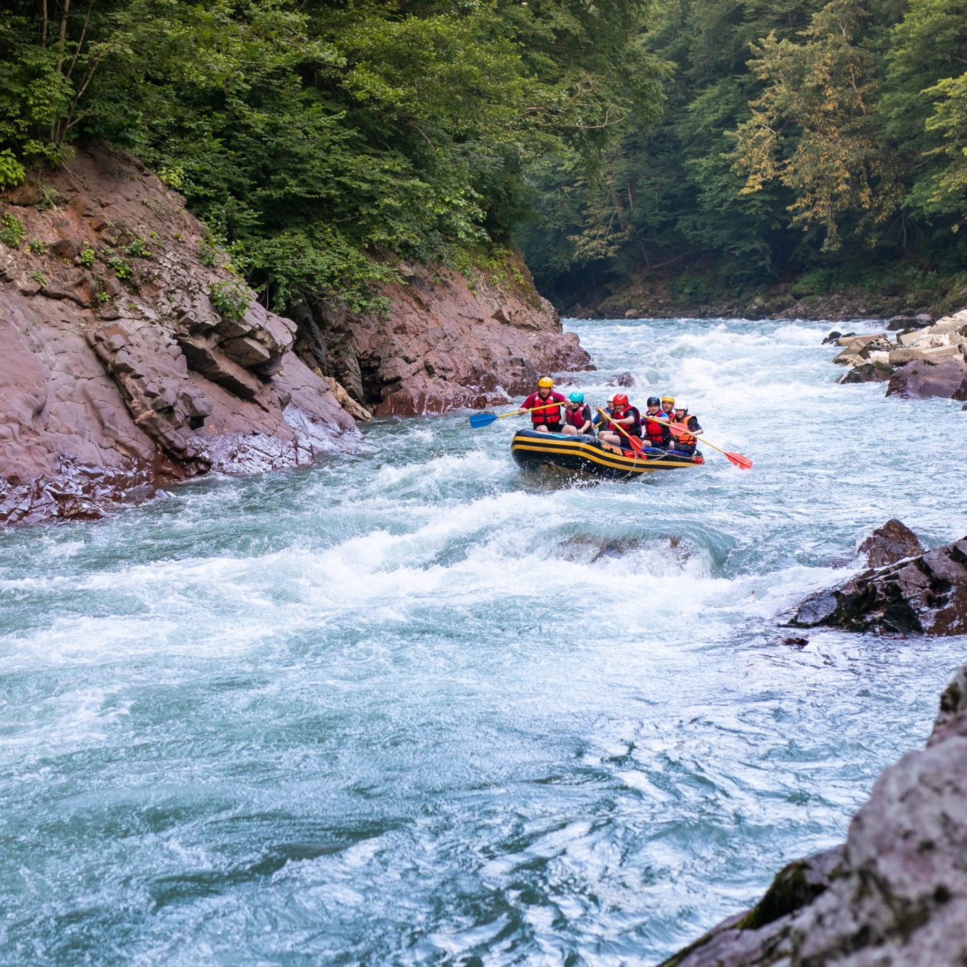 Group of happy people with guide whitewater rafting and rowing on river.